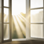 Offenes Fenster mit warmem Morgenlicht und sanften Vorhängen – ein Symbol für das Loslassen von Anspannung und einen ruhigen Neuanfang.